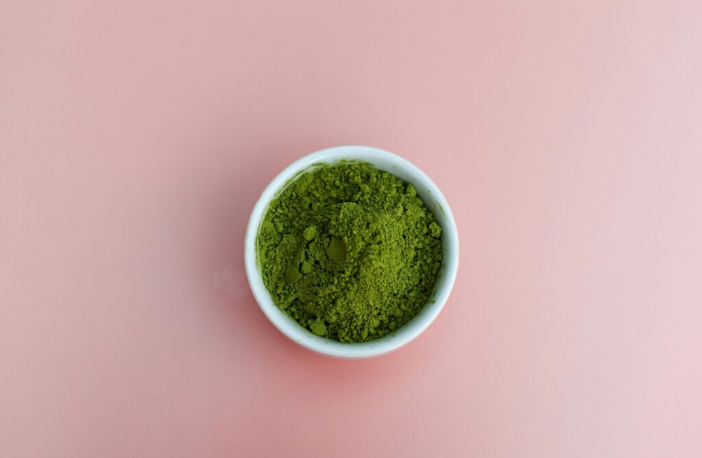 A white bowl holding kratom powder on a pink surface